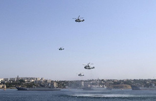 Russian military helicopters fly in formation, with warships seen on the water, during celebrations for Navy Day in the Black Sea port of Sevastopol