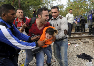 A migrant reacts as he carries a child during clashes with Macedonian police at the Greek-Macedonian border, August 21, 2015. Macedonian police drove back crowds of migrants and refugees trying to enter from Greece on Friday after a night spent stranded in no-man's land by an emergency decree effectively sealing the Macedonian frontier. A Reuters reporter said tear gas was fired and saw at least four bloodied migrants taken for treatment on the Greek side of the border..  REUTERS/Alexandros Avramidis