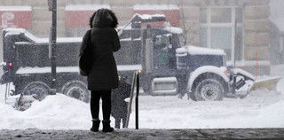 A woman waits for a ride as a snow plow passes in Boston, Thursday, Jan. 4, 2018. Forecasts for the Boston area call for about a foot of snow during the day and blizzard-like conditions. (AP Photo/Charles Krupa)